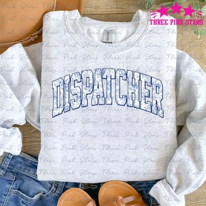 Op de afbeelding: Een grijs sweatshirt met het woord "DISPATCHER" bedrukt in blauw met een wit bloemenpatroon. Het woord is gebogen en heeft een blauwe omtrek.
