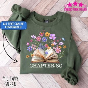 May include: Military green sweatshirt with a floral and book design. The graphic features an open book with colorful flowers and the text "CHAPTER 80". The text "ALL TEXT CAN BE CUSTOMIZED" is also visible.