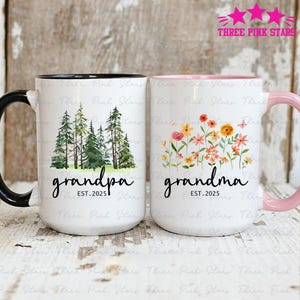 Peut inclure: Deux mugs en céramique blancs. L'un a une anse noire et présente une scène de forêt avec le mot "grandpa" et "EST. 2025". L'autre a une anse rose et présente un motif floral avec le mot "grandma" et "EST. 2025".