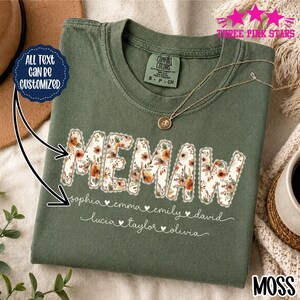 Könnte beinhalten: Ein olivgrünes T-Shirt mit dem Wort MEMAW in einem Blumenmuster mit gewelltem Rand. Unter dem Wort sind die Namen Sophia, Emma, Emily, David, Lucia, Taylor und Olivia in weißer Schreibschrift gedruckt, getrennt durch kleine weiße Herzen.