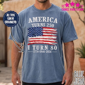 Op de afbeelding: Een spijkerblauw t-shirt met korte mouwen en een afbeelding van een verweerde Amerikaanse vlag met de tekst AMERICA TURNS 250, I TURN 80 en 1776-1946-2026. Een donkerblauwe ronde badge links vermeldt ALL TEXT CAN BE CUSTOMIZED.