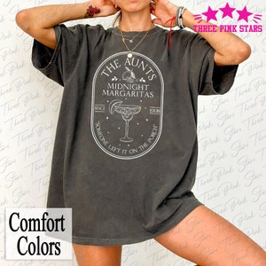 May include: A grey t-shirt with a white graphic design that says "The Aunts Midnight Margaritas Since 1998 Someone Left It On The Porch".