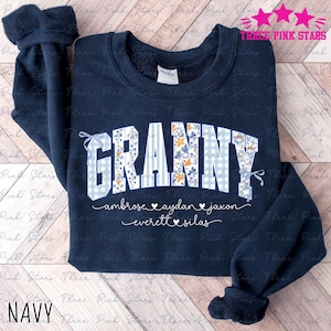 May include: Navy blue sweatshirt with the word "GRANNY" in a mix of floral, gingham, and striped patterns. Below the word are names and hearts. The text "THREE PINK STARS" is at the top right. The word "NAVY" is at the bottom left.