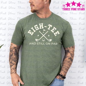 May include: A green t-shirt with a white graphic that says "Eigh-Tee and Still on Par" with a golf club and ball design.