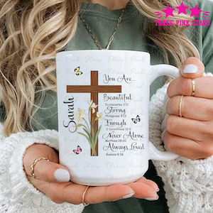 May include: White ceramic mug featuring a wooden cross, floral accents, and the name "Sarah." The mug includes inspirational text: "You Are... Beautiful, Strong, Enough, Never Alone, Always Loved." Butterflies decorate the design.