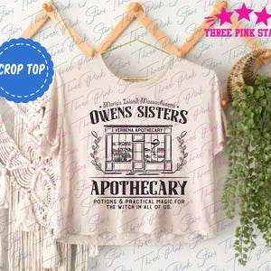 May include: A cream-coloured crop top featuring the words "Owens Sisters Apothecary" in black. The design includes an illustration of a storefront and the words "Potions & Practical Magic for the Witch in All of Us."