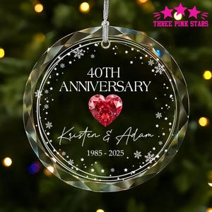 May include: A clear, faceted glass ornament with the text "40TH ANNIVERSARY" and a red heart. The names "Kristen & Adam" and the years "1985-2025" are also displayed. The ornament is hanging from a silver string.