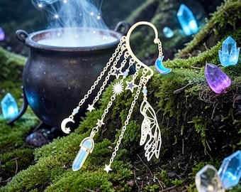 May include: A gold-colored ear cuff with celestial charms, including moons, stars, and a crystal pendant. The cuff is set against a backdrop of moss, crystals, and a bubbling cauldron, creating a mystical aesthetic.