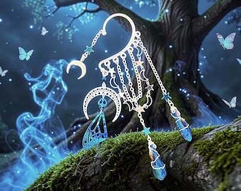May include: Silver ear cuff featuring crescent moons, stars, and dangling blue crystal accents. The cuff includes a blue butterfly wing design and is set against a mystical forest backdrop with butterflies and a full moon.