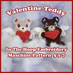 May include: Two plush teddy bears with angel wings holding red hearts. The bears are in front of a blue and white background with snowflakes. The text "Valentine Teddy In The Hoop Embroidery Maschine Pattern 5 x 7" is at the bottom of the image.