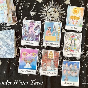May include: A set of ten tarot cards from the Wonder Water Tarot deck. The cards are laid out on a black background with a star pattern. The cards feature watercolor illustrations and include the Lovers, Eight of Pentacles, the Sun, the Magician, Two of Pentacles, Five of Pentacles, and Seven of Cups.