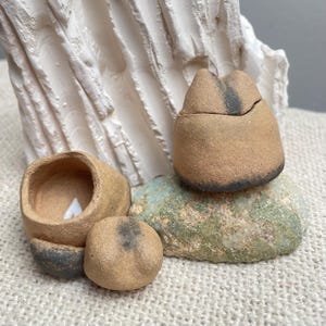 Peut inclure: Deux petites boîtes en céramique à couvercle avec un glaçage rustique brun. Les boîtes sont posées sur un rocher avec un glaçage vert et bleu.