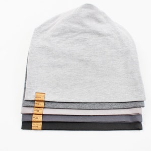 May include: Stack of six gray, charcoal, and black beanie hats with a brown leather label that says "mos" on each hat.