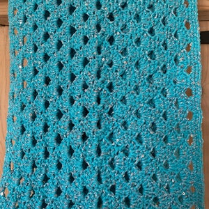 Op de afbeelding: Een turquoise gehaakte deken met zilveren pailletten. De deken heeft een ruitpatroon en is gemaakt van zacht garen.