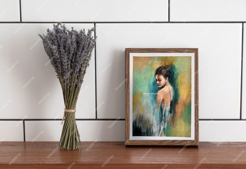 May include: A framed painting of a woman with brown hair, wearing a blue and white dress, against a yellow and green background. The painting is in a brown frame and is on a wooden surface.