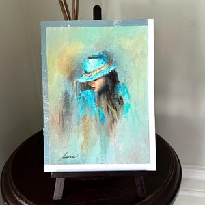 May include: A painting of a woman wearing a light blue hat and a light blue jacket. The background is a soft, abstract blend of light blue, green, and yellow.