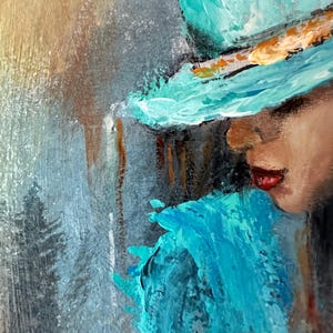 May include: A painting of a woman wearing a teal blue hat with a gold band. The woman's face is partially obscured by the hat, and she is looking down. The background is a blurry, abstract painting of teal blue and gray.