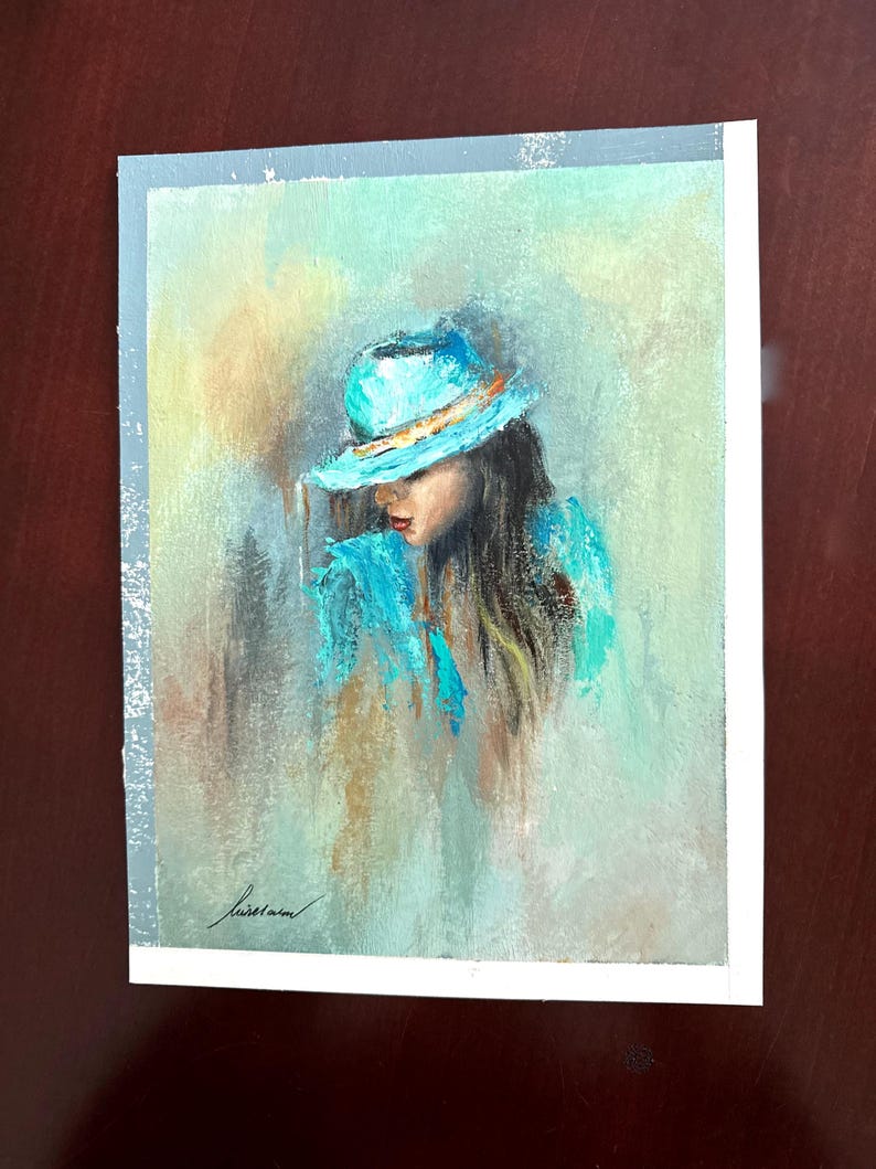 May include: A painting of a woman wearing a blue hat and a blue shirt. The background is a soft, abstract blend of colors.