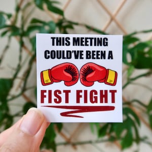 Peut inclure: Autocollant blanc avec le texte "This meeting could've been a fist fight" en noir. Deux gants de boxe rouges avec des poignets jaunes sont représentés au-dessus du texte.