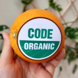 May include: A sticker with a brown border and a white background. The sticker has green text that says "CODE ORGANIC" with a green and white striped design.