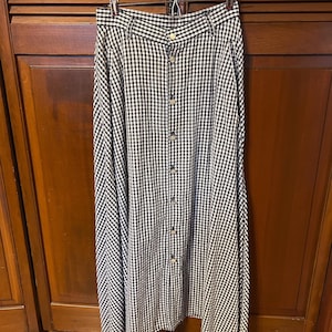 May include: A long, black and white gingham skirt with a button-down front. The skirt is hanging on a metal hanger. The fabric has a classic checkered pattern. The skirt is a midi length.