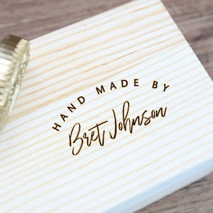 Puede incluir: Una caja de madera con un sello de latón que dice "HAND MADE BY Bret Johnson".