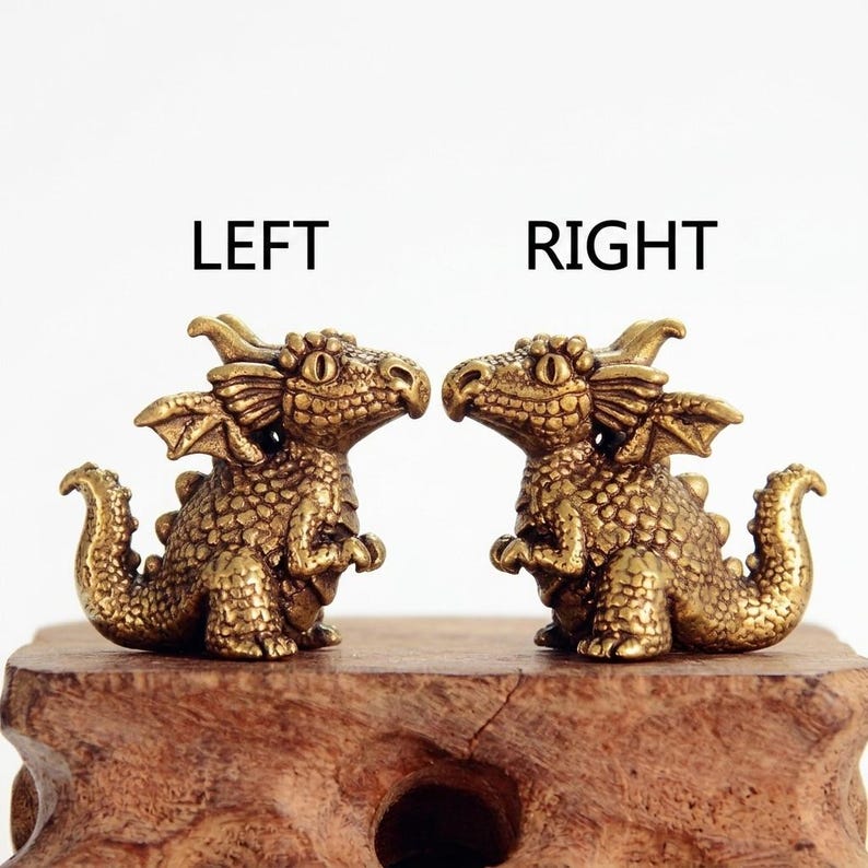 K&ouml;nnte beinhalten: Zwei kleine, detaillierte Drachenfiguren aus Messing mit strukturierten Schuppen, Fl&uuml;geln und H&ouml;rnern. Der linke Drache blickt nach rechts, der rechte Drache nach links. &Uuml;ber den Figuren steht der Text LEFT beziehungsweise RIGHT.