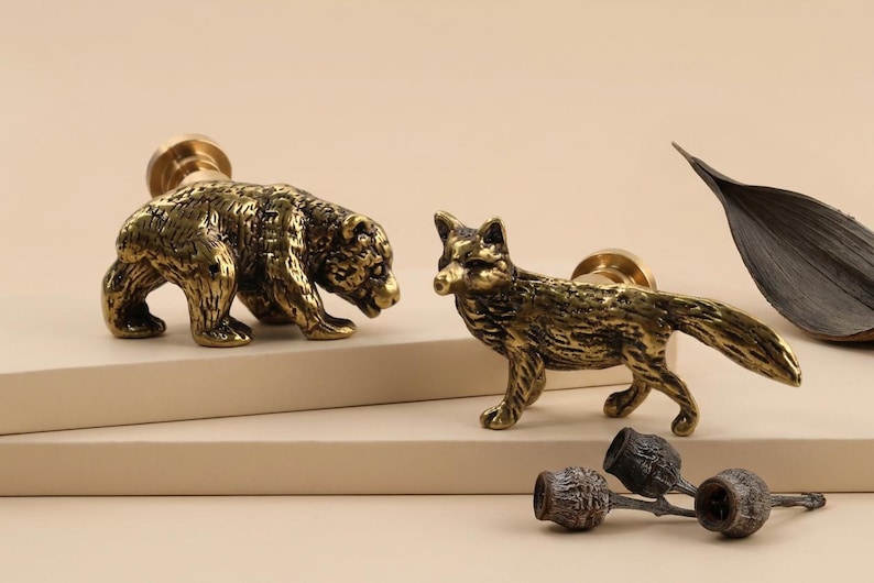 May include: Two brass animal-shaped cabinet knobs: a bear and a fox. The bear is on all fours, and the fox is standing. The knobs have a vintage, antique appearance. A few decorative elements are also present.