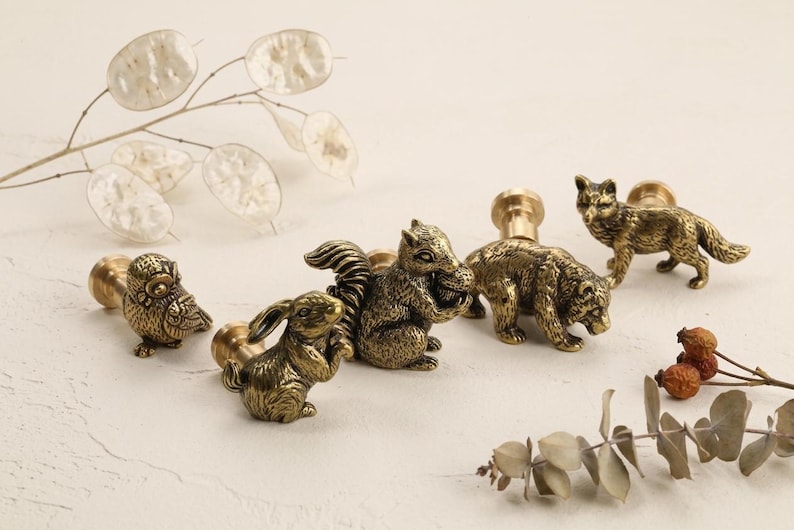 May include: A collection of antique brass animal cabinet knobs, including an owl, rabbit, squirrel, bear, and fox. These decorative knobs add a rustic, woodland touch to furniture and are perfect for a nature-themed decor.