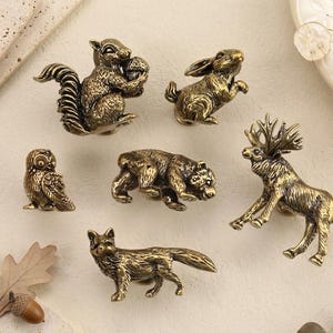 May include: A collection of bronze-colored animal figurines, including a squirrel, rabbit, owl, bear, deer, and fox. The detailed figures are arranged on a neutral surface, suggesting a decorative or collectible theme.