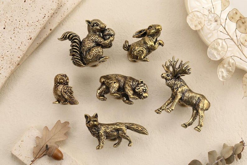 May include: A collection of bronze-colored animal figurines, including a squirrel, rabbit, owl, bear, deer, and fox. The detailed figures are arranged on a neutral surface, suggesting a decorative or collectible theme.