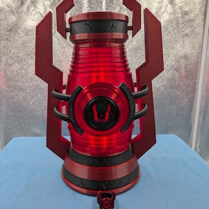 May include: A red and black lantern featuring a translucent red cylindrical body, a black handle, and a central circular emblem. The base and top sections are black with a cracked texture, and the frame consists of angular red side supports.