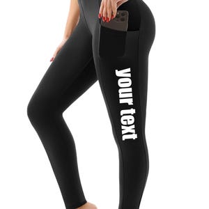 May include: Black high-waisted leggings featuring a side pocket and the white text 'your text' printed vertically along the left leg. The leggings have a fitted silhouette and a smooth, solid-coloured fabric construction throughout the design.