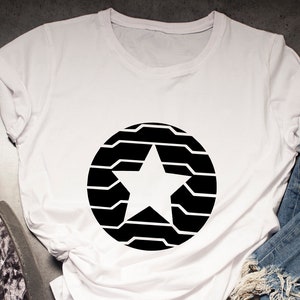 Puede incluir: Camiseta blanca con un dise&ntilde;o de estrella negra dentro de un c&iacute;rculo, combinada con vaqueros azules y zapatillas estampadas. Un reloj, gafas y un smartphone con auriculares completan el conjunto informal.