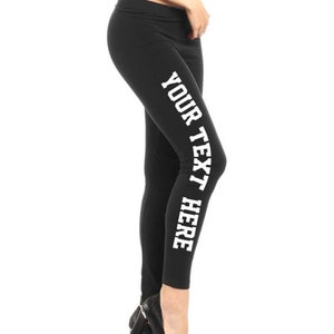 May include: Black leggings with the text "YOUR TEXT HERE" printed vertically in white on the left leg. The leggings are worn with black high-heeled shoes. The image is set against a white background.