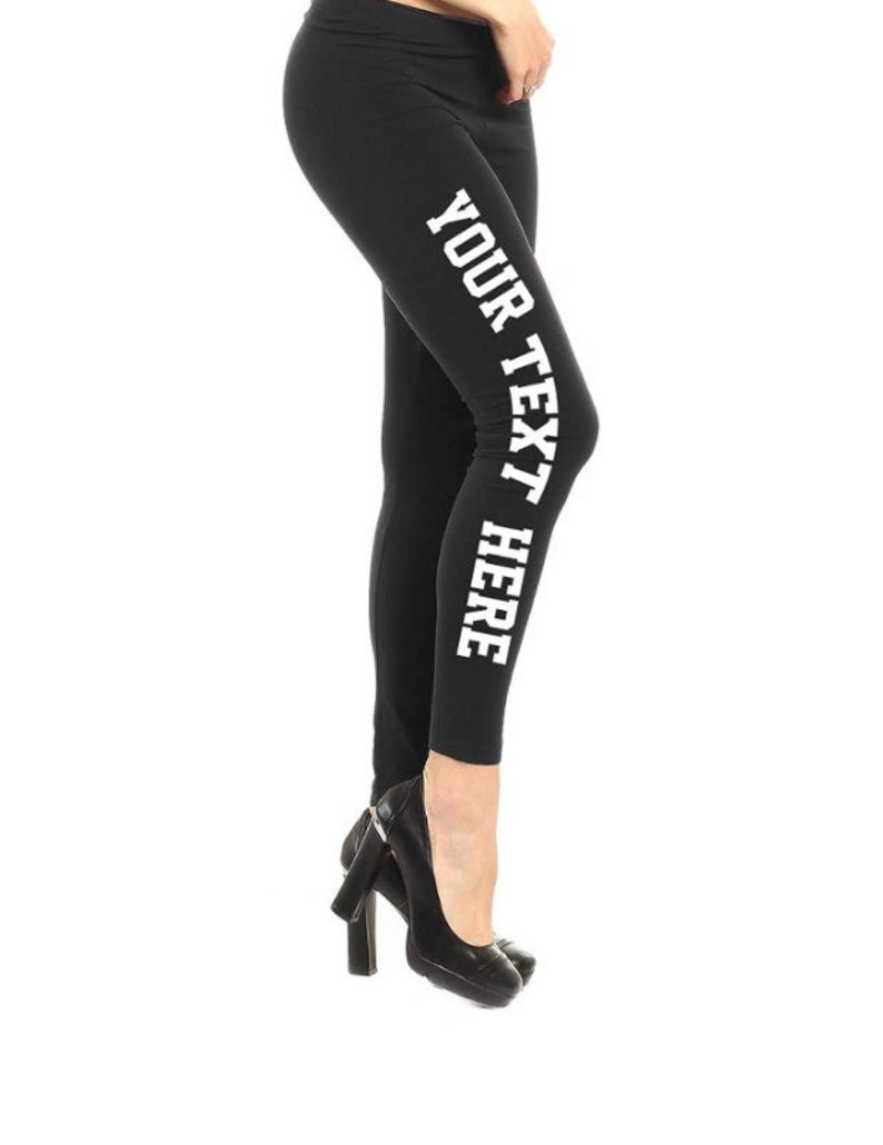 May include: Black leggings with the text "YOUR TEXT HERE" printed vertically in white on the left leg. The leggings are worn with black high-heeled shoes. The image is set against a white background.