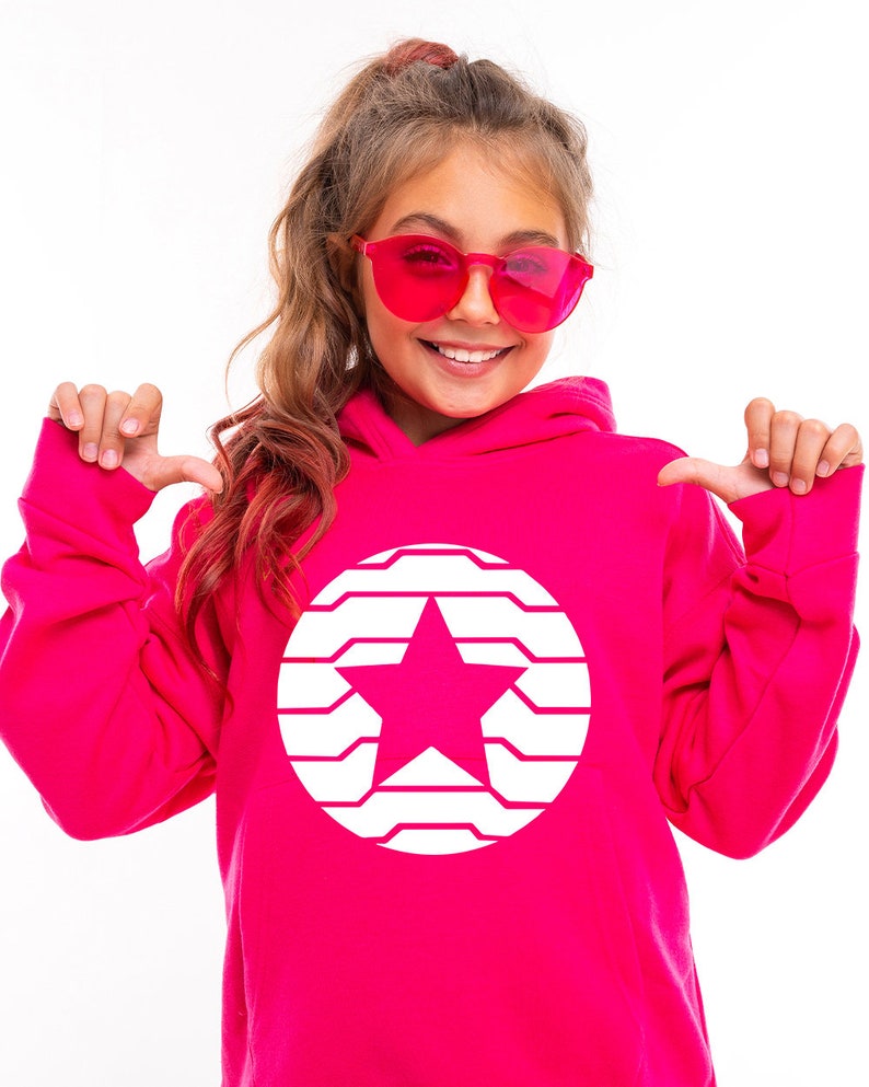 K&ouml;nnte beinhalten: Ein leuchtend pinkfarbener Kapuzenpullover mit einem wei&szlig;en Stern-Design in einem Kreis. Die Person im Bild tr&auml;gt eine rosa Sonnenbrille und zeigt auf den Hoodie. Ein auff&auml;lliges Kleidungsst&uuml;ck.