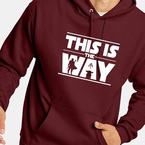 Puede incluir: Sudadera con capucha burdeos con un gr&aacute;fico blanco que dice "THIS IS THE WAY" con siluetas de un personaje y una criatura. La sudadera tiene una capucha con cord&oacute;n y un bolsillo delantero.