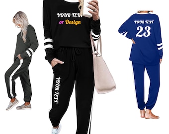 Pode incluir: Conjuntos de roupa de descanso de três peças em preto, cinza carvão e azul. Cada conjunto inclui uma parte superior de manga comprida e calças a condizer com uma faixa branca na lateral. O conjunto preto tem o texto "YOUR TEXT or Design" na parte superior e nas calças. O conjunto azul tem o número 23 nas costas.