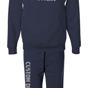 Pode incluir: Conjunto de moletom com capuz e cal&ccedil;as de moletom azul marinho. O moletom tem um bolso frontal e o texto "CUSTOM DESIGN" impresso na frente. As cal&ccedil;as de moletom tamb&eacute;m t&ecirc;m o texto "CUSTOM DESIGN" impresso verticalmente na perna esquerda.
