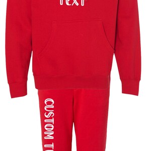 Pode incluir: Conjunto vermelho de moletom com capuz e cal&ccedil;as de moletom. O moletom tem um bolso frontal e um capuz com cord&atilde;o. O texto "CUSTOM TEXT" &eacute; impresso na frente do moletom e na perna esquerda.