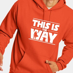 Puede incluir: Sudadera con capucha naranja con un gr&aacute;fico blanco que dice "THIS IS THE WAY" con siluetas de un Mandaloriano y Grogu. La sudadera tiene un bolsillo delantero y una capucha con cord&oacute;n.