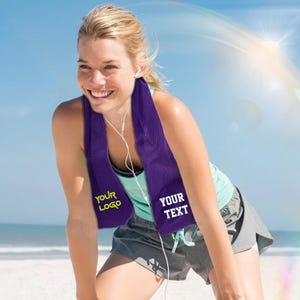 May include: A purple cooling towel with the text "YOUR LOGO" and "YOUR TEXT" in yellow and white. The towel is around the neck of a person wearing a teal vest and grey shorts. The person is smiling, with earphones in.