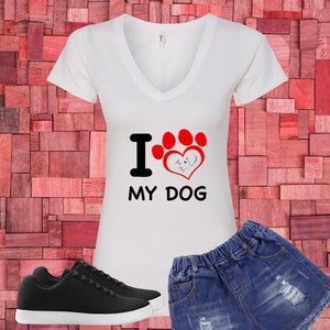 May include: White V-neck t-shirt with the text "I LOVE MY DOG" and a paw print design. Includes black sneakers and denim shorts. The shirt features a red paw print and a heart with a dog silhouette.