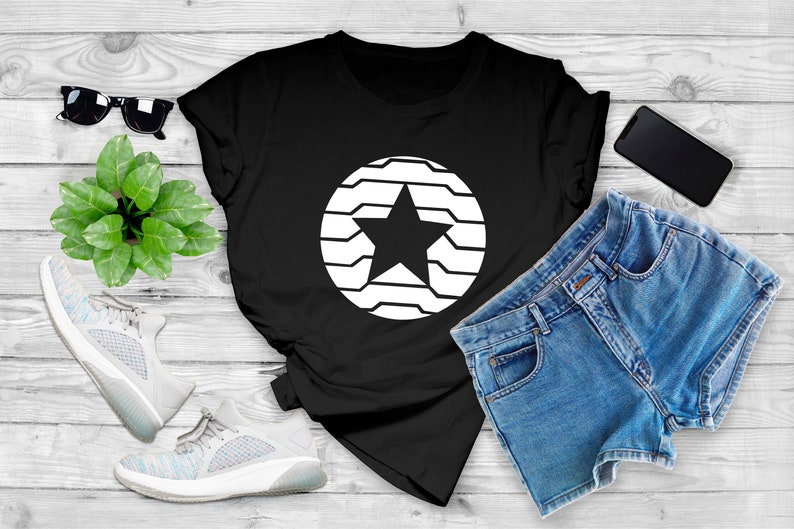 Puede incluir: Camiseta negra con un dise&ntilde;o de estrella blanca dentro de un c&iacute;rculo. La imagen tambi&eacute;n incluye pantalones cortos de mezclilla, gafas de sol, un tel&eacute;fono inteligente y zapatillas deportivas, con una peque&ntilde;a planta en una superficie de madera.