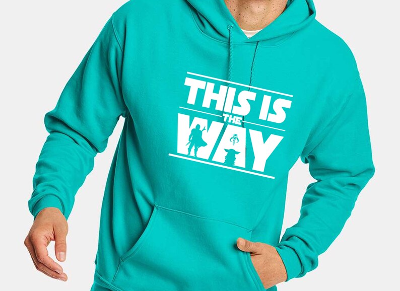Puede incluir: Sudadera con capucha turquesa con la frase blanca "THIS IS THE WAY" y siluetas de personajes. La sudadera tiene un bolsillo delantero y una capucha con cord&oacute;n.