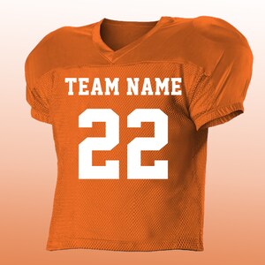 Peut inclure: Maillot de football am&eacute;ricain orange avec lettrage et chiffres blancs. Le maillot affiche le texte "TEAM NAME" au-dessus du num&eacute;ro "22". Il poss&egrave;de un col en V et des &eacute;paules rembourr&eacute;es.
