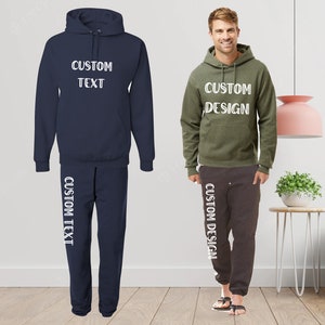 Pode incluir: Conjunto de moletom azul marinho e cal&ccedil;as de moletom combinando com o texto "CUSTOM TEXT" em branco. Um segundo conjunto em verde oliva e cinza carv&atilde;o com o texto "CUSTOM DESIGN" tamb&eacute;m &eacute; mostrado. Ambos os conjuntos s&atilde;o exibidos em um piso de madeira clara.
