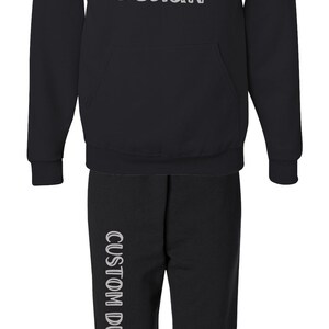 Pode incluir: Conjunto preto de moletom com capuz e cal&ccedil;as de moletom. O moletom tem um bolso frontal e um capuz com cord&atilde;o. O texto "CUSTOM DESIGN" &eacute; impresso na frente do moletom e na lateral das cal&ccedil;as.