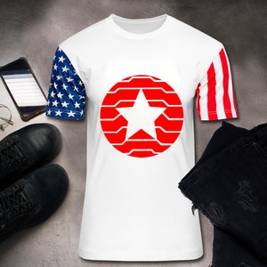 Puede incluir: Camiseta blanca con un dise&ntilde;o de estrella roja dentro de un c&iacute;rculo rojo. La manga izquierda tiene un patr&oacute;n de estrellas azules y blancas, y la manga derecha tiene rayas rojas y blancas. Botas negras, vaqueros, reloj, gafas y tel&eacute;fono.